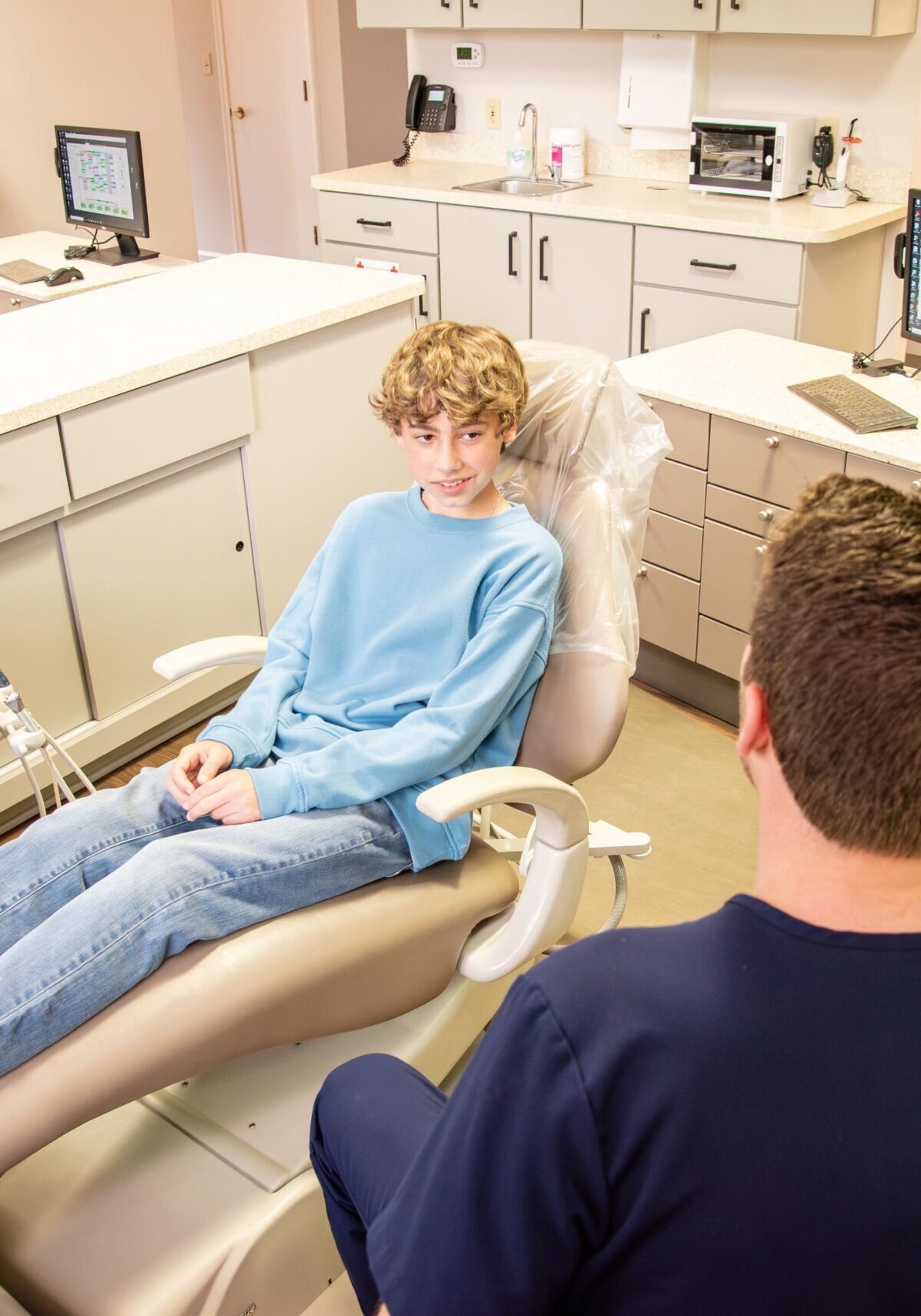 Teen male patient sitting in chair, talking to doctor